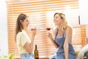 Female couple preparing meal together and drinking wine. Lesbian couple, champagne and LGBTQ with happy smile, love and cooking in kitchen and hosting a party in home. photo