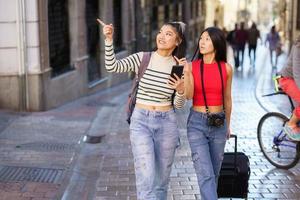 Asian female travelers pointing away while walking on street photo