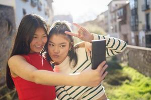 Smiling Asian girlfriends taking selfie on street photo