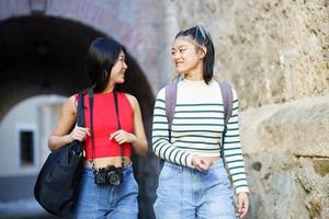 Cheerful Asian women walking near stone wall photo