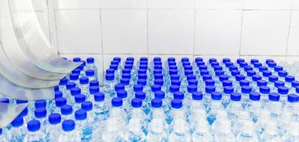 Lots of water bottles. Bottles with blue caps. Bottling plant-Water bottling line for processing and bottling drink water into bottles. photo