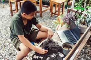 Boy learns to grow flowers in pots through online teaching. shoveling soil into pots to prepare plants for planting leisure activities concept photo