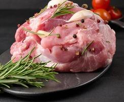 A piece of pork ham on a black board and spices olive oil, salt, rosemary branch and pepper photo