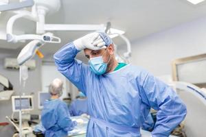 tenso cirujano con manos en cara en operando habitación en hospital. agotado cirujano después largo cirugía foto