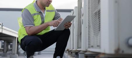 Asian maintenance engineer works on the roof of factory. contractor inspect compressor system and plans installation of air condition systems in construction. technology, online checking photo