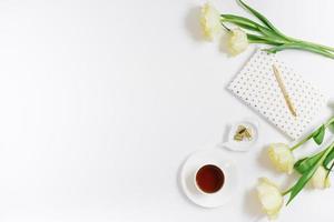 The blogger's spring flat lay. White notepad, pen, bouquet of yellow tulips and a cup of tea on a white background with copy space photo