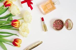 Red and yellow tulips in a red gift bag, cosmetics and gift on a white background with copying space. Greeting card for Valentine's Day or Mother's Day. Stylish blogger flat lay photo