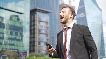 zakenman op zoek Bij telefoon winnen kans en zich verheugen. zakenman op zoek Bij zijn telefoon verheugt en wezen gelukkig Aan de stad straat. video