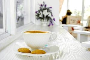 caliente latté café en un blanco café taza con galletas en blanco de madera mesa. foto