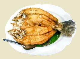 Top view of fried snapper fish topped with fish sauce on banana leaf and white ceramic plate with stainless steel spoon., This food is most popular Thai food in the restaurant. photo