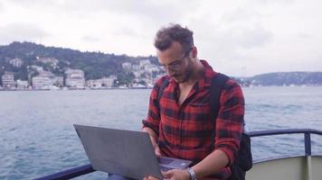Mens werken Aan laptop Aan veerboot. gelukkig en tevreden. Mens aan het doen zijn werk Aan laptop tegen stadsgezicht. hij is gelukkig en inhoud met zijn leven. video