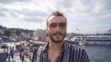 Young Man is looking at the sky against the sea in Istanbul. Handsome young man is stylish and wearing sunglasses and stands against the sea. video