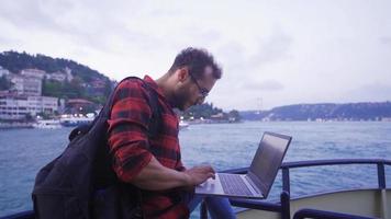 homem trabalhando em computador portátil em balsa. a homem assistindo a cidade a partir de 1 lado, trabalhando dentro dele computador portátil em a balsa. video