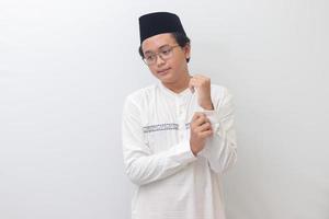 retrato de joven asiático musulmán hombre molesto a reparar su camisa botones. aislado imagen en blanco antecedentes foto