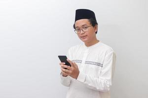 Portrait of young Asian muslim man holding mobile phone with smiling expression on face. Isolated image on white background photo