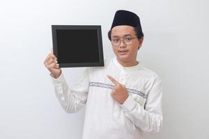 Portrait of young Asian muslim man holding a blackboard with hand pointed. Blank space for typography or text to fill. Isolated image on white background photo