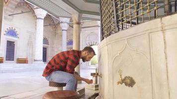 musulmán joven hombre realiza ablución en el fuente. un hombre ejecutando ablución en el patio de el mezquita. video