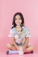 A little girl in a white dress is sitting near the window and holding a rose. A happy child at the window with a flower. photo