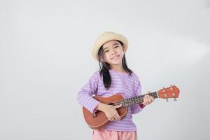 linda pequeño niña en traje de baño jugando ukelele contento vacaciones concepto. foto