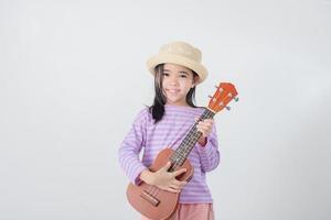 linda pequeño niña en traje de baño jugando ukelele contento vacaciones concepto. foto