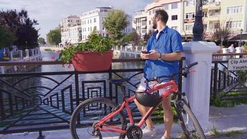 Young man texting on the phone. Young man standing by the river passing through the city, texting on his phone. video