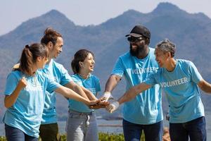 equipo de joven y diversidad voluntario trabajador grupo disfrutar Caritativo social trabajo al aire libre juntos en ahorro ambiente proyecto vistiendo azul camiseta mientras unión mano en poder montar unidad concepto foto