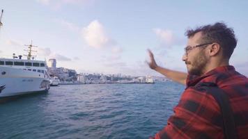 Young man waving from the ferry. Happy. The man waving goodbye from the ferry running through the Bosphorus in the cityscape. video