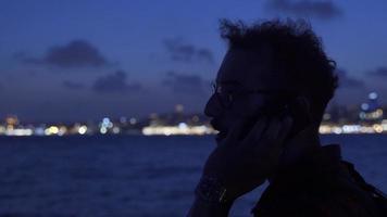 uomo parlando su il Telefono su il traghetto a notte. scuro. uomo parlando su il Telefono contro il città a notte. silhouette. video