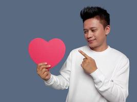 Man holding and pointing red heart shape isolated on plain background. photo