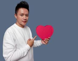 Man holding and pointing red heart shape isolated on plain background photo