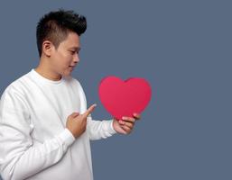 Man holding and pointing red heart shape isolated on plain background photo