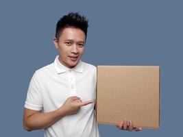 Young man showing cardboard box and pointing isolated on plain background photo