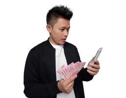 Handsome man with surprised facial expression looking at mobile screen and holding indonesian money photo