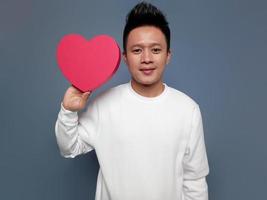 Handsome man showing red heart shape isolated on plain background photo