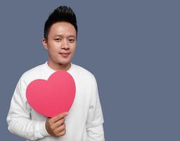 Handsome man holding and showing red heart shape with one hand. photo