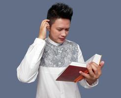 Confused expression of muslim man holding Al Quran while scratching head photo