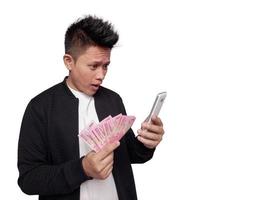 Handsome man with surprised facial expression looking at mobile screen and holding indonesian money photo