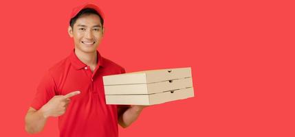 The smiling pizza delivery man stands on a red background holding the pizza box and wearing a red cap and a blank t-shirt uniform. photo