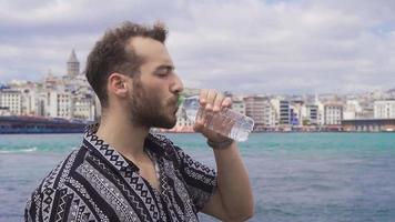 el hombre Bebiendo agua por el mar en Estanbul. joven hombre Bebiendo agua por el mar y siendo contento. video