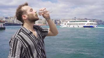 Mens drinken water Aan de strand door de zee. Mens drinken water door de zee in Istanbul en de stad campus en galata toren in de achtergrond. video