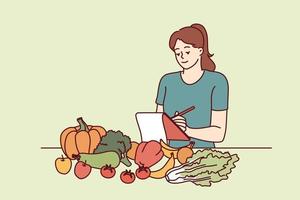 mujer nutricionista es en pie cerca mesa con vegetales y haciendo notas en computadora portátil, haciendo plan para nuevo dieta a desintoxicar cuerpo. niña nutrición especialista usos Lista de Verificación a marca dieta ingredientes vector