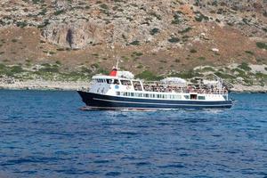 blanco turista Embarcacion con turistas es navegación algun lado en el mar en contra el fondo de montañas y un playa foto