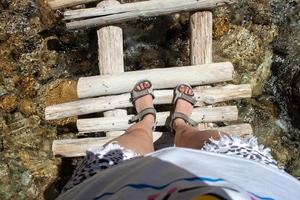 hermosa piernas de un viajero en un de madera puente por el río después un caminata en el montañas. viaje y libertad concepto foto