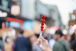 woman hand holding caramel coated strawberry skewer at night market. Street Food and travel concept photo