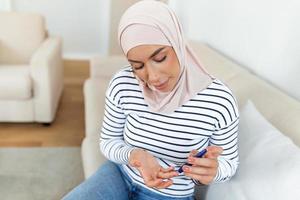 joven Arábica musulmán mujer medidas sangre azúcar nivel. diabetes utilizando glucómetro foto