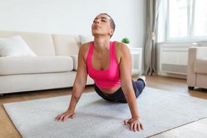 Relief Lower Back Pain. Smiling Black Woman Doing Sphinx Cobra Pose Or Upward-Facing Dog Asana Stretching Back Muscles Practicing Pilates, Excercising At Fitness Studio Or In Living Room On Yoga Mat photo