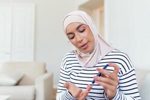 Arábica mujer utilizando lanceta en dedo para comprobación sangre azúcar nivel por glucosa metro, cuidado de la salud y médico, diabetes, glicemia concepto foto