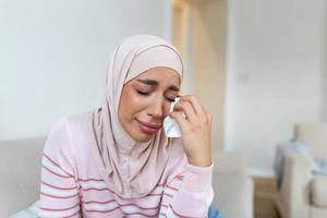 Young Muslim woman sitting in room feeling pain with life problem. Crying muslim female holding painful hand, suffering from husband violence photo