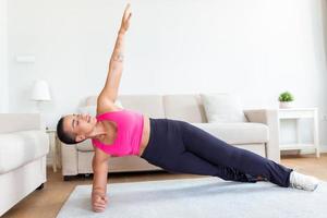 Full Body Length Of Happy Fit African American Woman Exercising On Yoga Mat Standing In Side Plank Position Near Window photo