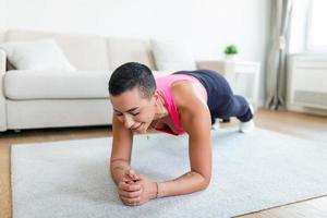 Healthy Lifestyle Concept. African American Lady Standing In Plank Position On Yoga Mat At Home Or Fitness Studio. Cheerful Female In Sportswear Training Core And Abs Muscles photo